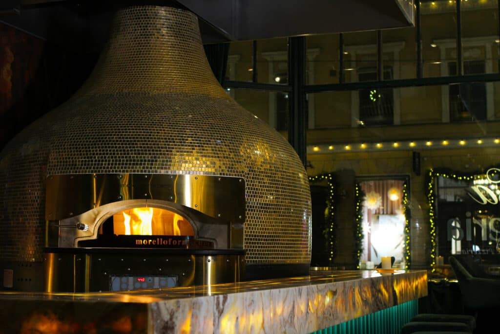 Italialainen puulämmitteinen pizzauuni jossa palaa tuli.